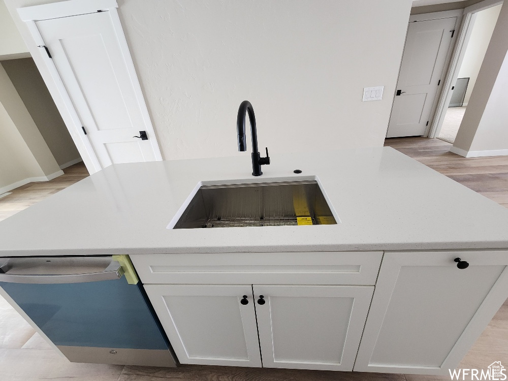 Kitchen with white cabinetry, light wood-type flooring, light stone counters, sink, and dishwasher