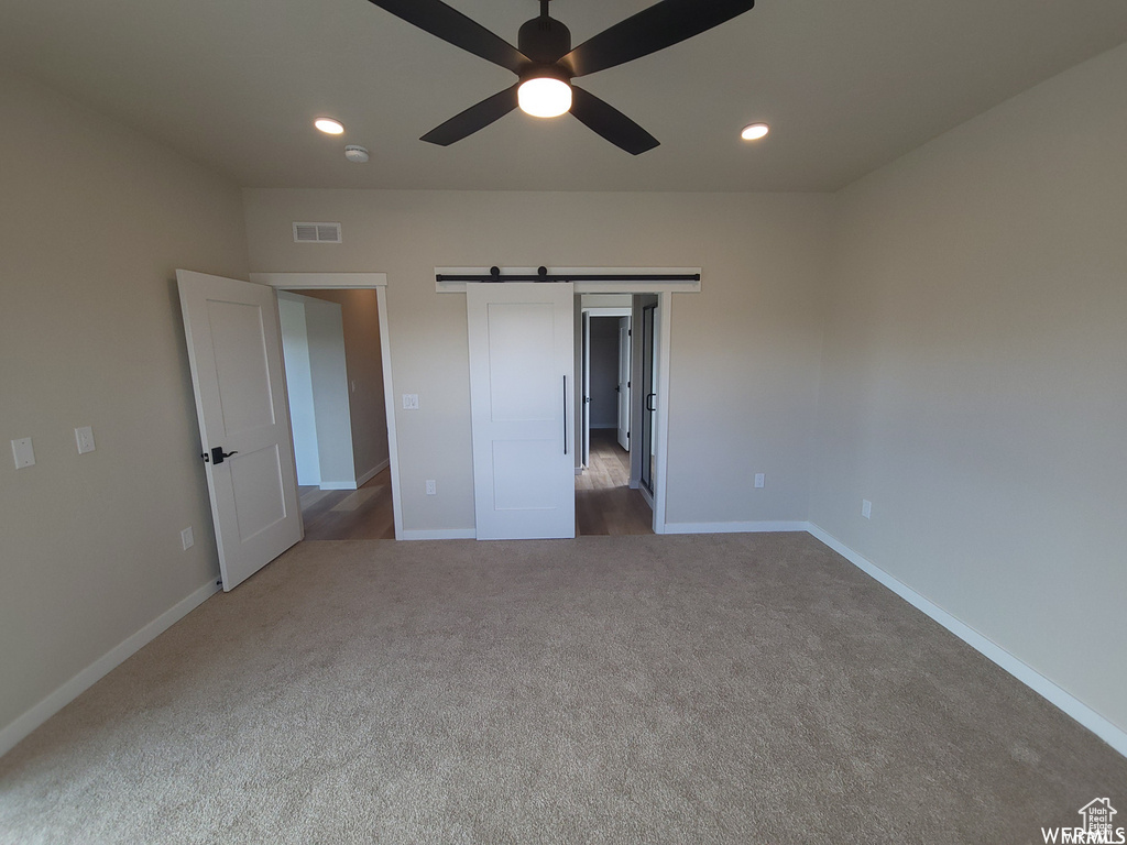 Unfurnished bedroom featuring a barn door, carpet, and ceiling fan