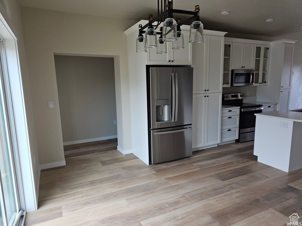 Kitchen featuring a notable chandelier, white cabinetry, light wood-type flooring, appliances with stainless steel finishes, and pendant lighting