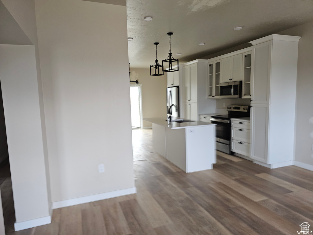 Kitchen with white cabinetry, a center island with sink, stainless steel appliances, decorative light fixtures, and wood-type flooring