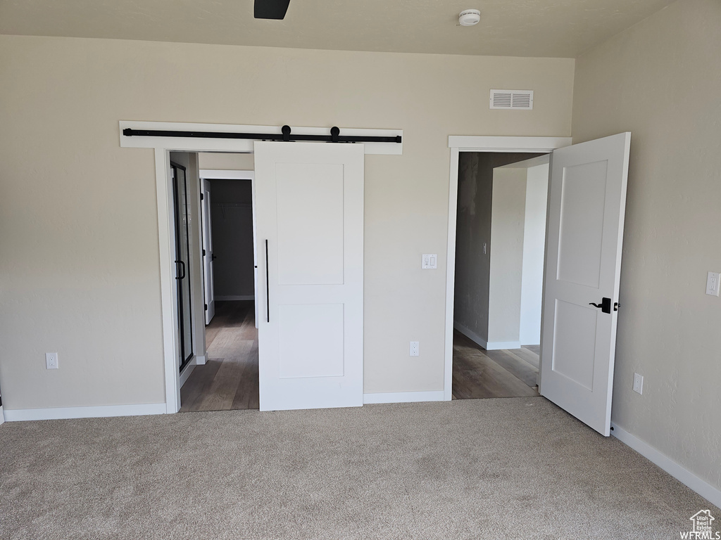 Unfurnished bedroom with a barn door and dark colored carpet