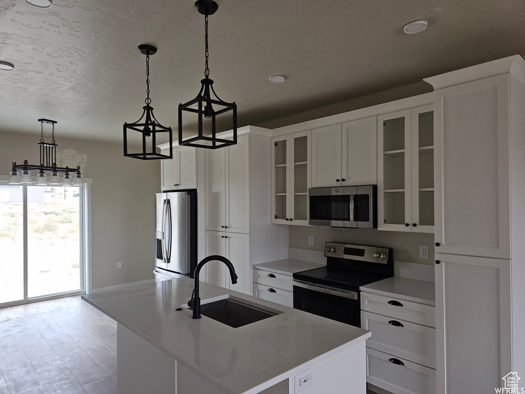 Kitchen featuring a center island with sink, pendant lighting, sink, white cabinets, and appliances with stainless steel finishes