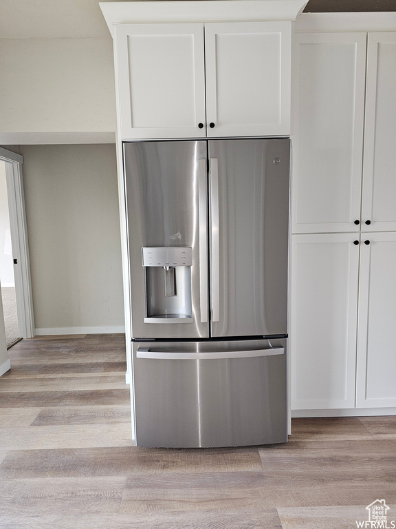 Kitchen with white cabinets, stainless steel fridge with ice dispenser, and light hardwood / wood-style flooring