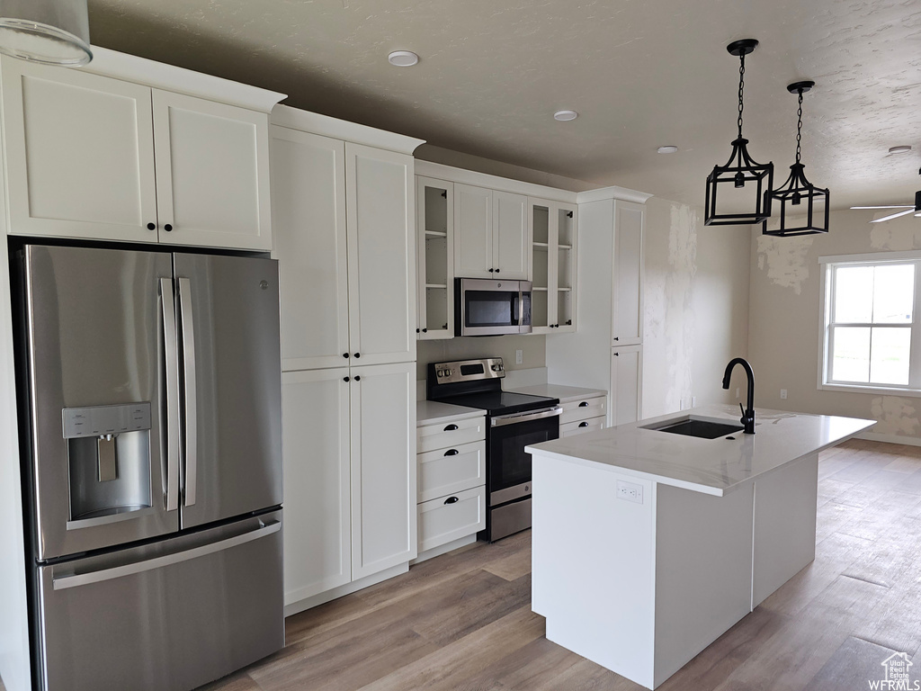 Kitchen with decorative light fixtures, light hardwood / wood-style floors, a center island with sink, white cabinetry, and appliances with stainless steel finishes