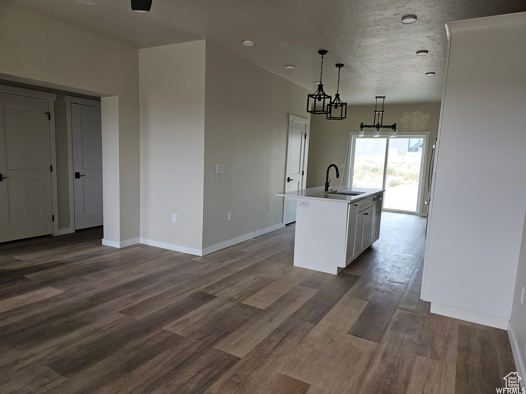 Kitchen featuring dark hardwood / wood-style floors, hanging light fixtures, an island with sink, white cabinets, and sink