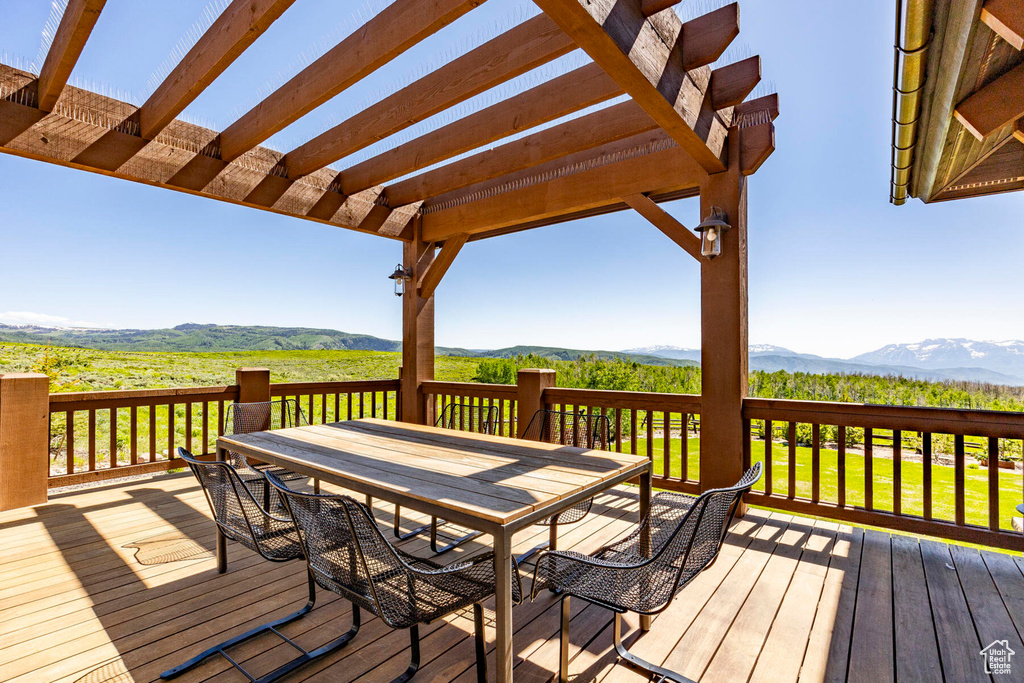 Wooden terrace with outdoor dining space, a mountain view, and a pergola