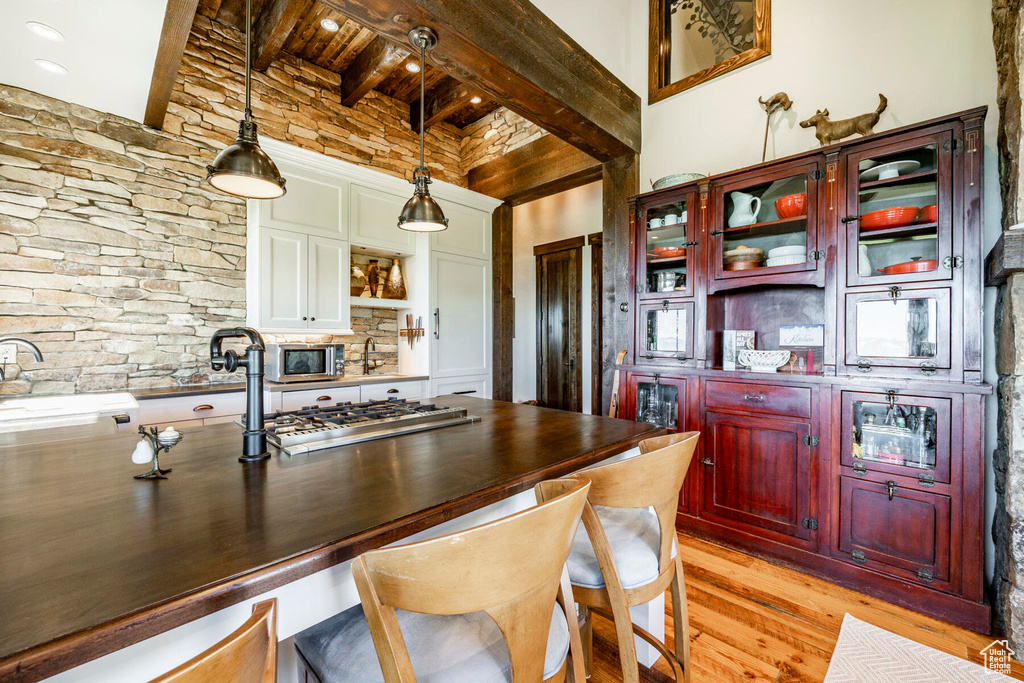 Kitchen featuring beam ceiling, stainless steel appliances, open shelves, light wood-style flooring, and reddish brown cabinets