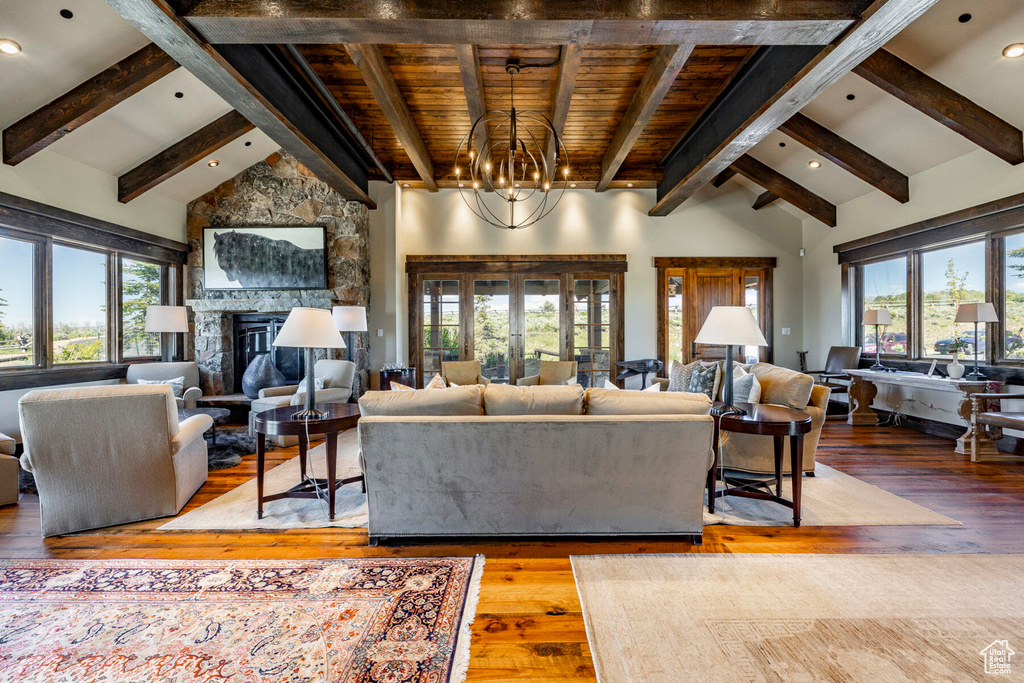 Living room with beam ceiling, hardwood / wood-style floors, a stone fireplace, a chandelier, and high vaulted ceiling