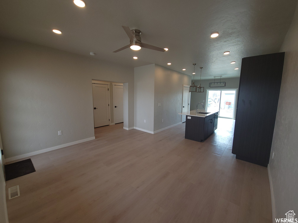 Unfurnished living room with ceiling fan, sink, and light wood-type flooring