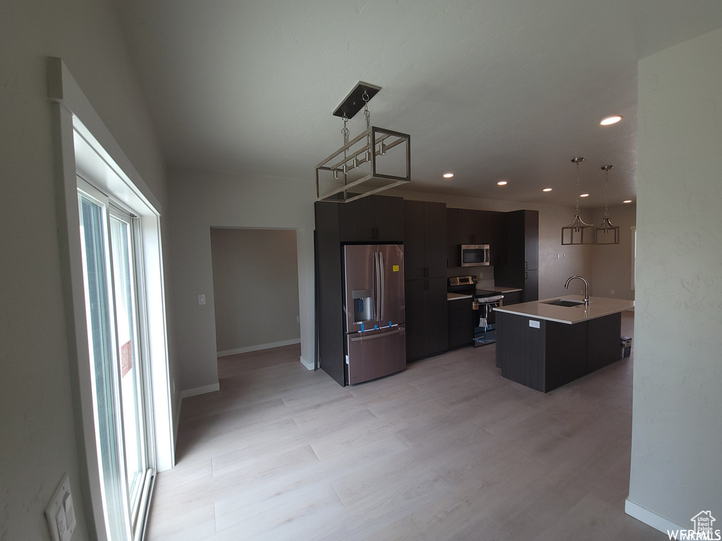 Kitchen featuring stainless steel appliances, hanging light fixtures, sink, and light wood-type flooring