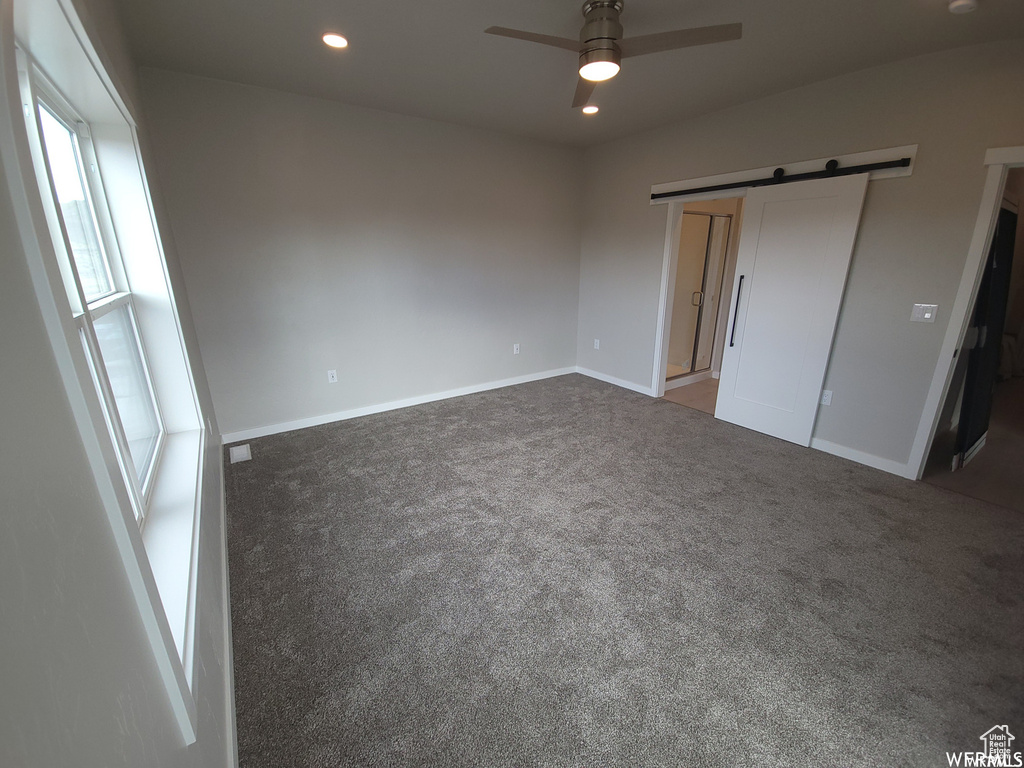 Unfurnished bedroom featuring carpet, ceiling fan, a closet, and a barn door