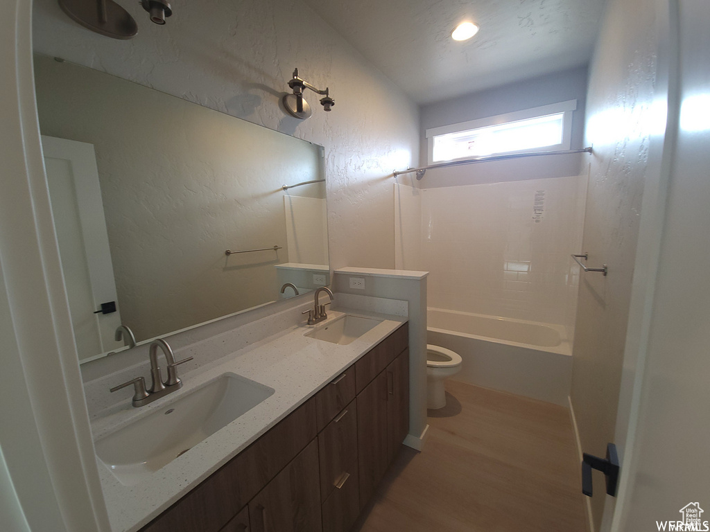 Full bathroom featuring double sink, vanity with extensive cabinet space, shower / tub combination, hardwood / wood-style flooring, and toilet