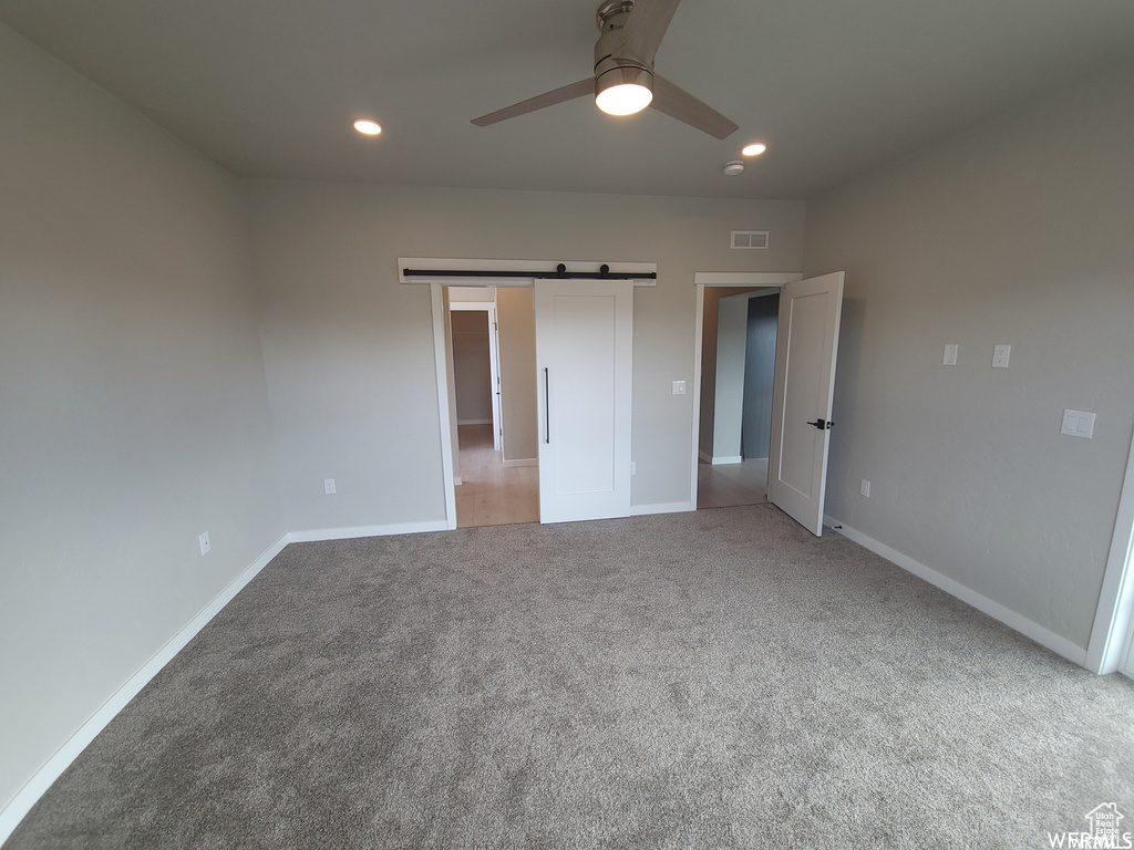 Unfurnished bedroom with a barn door, carpet flooring, and ceiling fan