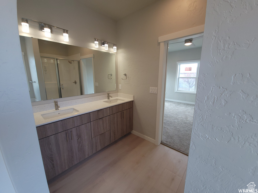 Bathroom featuring hardwood / wood-style floors, oversized vanity, double sink, and an enclosed shower