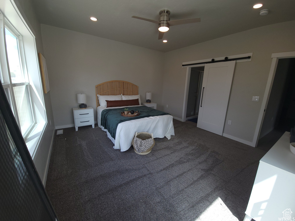 Bedroom featuring a barn door, a closet, dark colored carpet, and ceiling fan