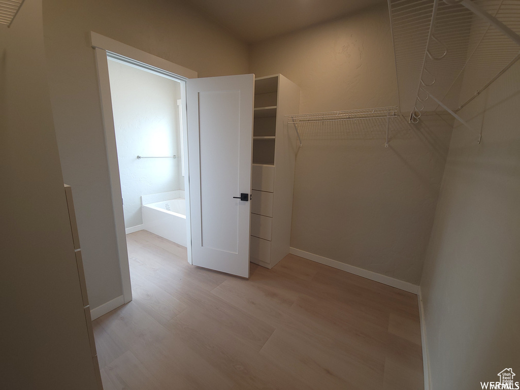 Walk in closet with light hardwood / wood-style floors