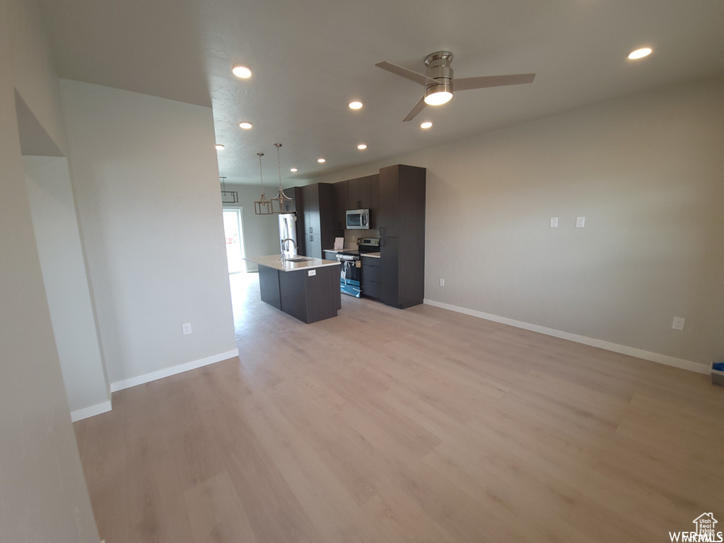 Kitchen featuring light hardwood / wood-style floors, stainless steel appliances, a center island with sink, ceiling fan, and sink