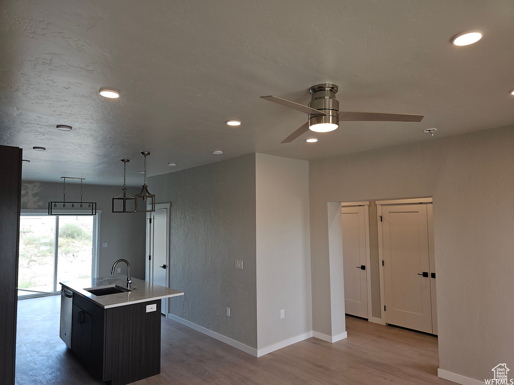 Kitchen with ceiling fan, a center island with sink, light wood-type flooring, pendant lighting, and sink