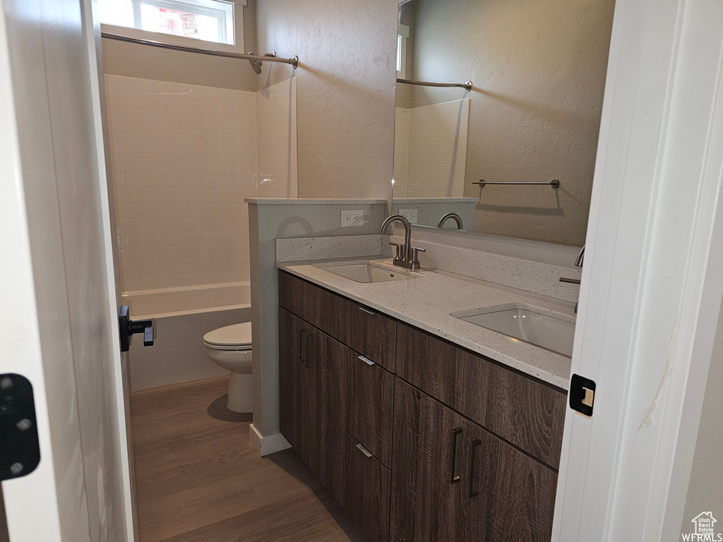 Full bathroom with hardwood / wood-style floors, double sink vanity, toilet, and tiled shower / bath