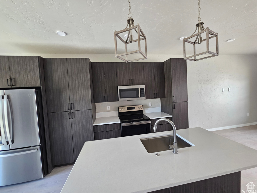 Kitchen with hanging light fixtures, stainless steel appliances, a center island with sink, and sink