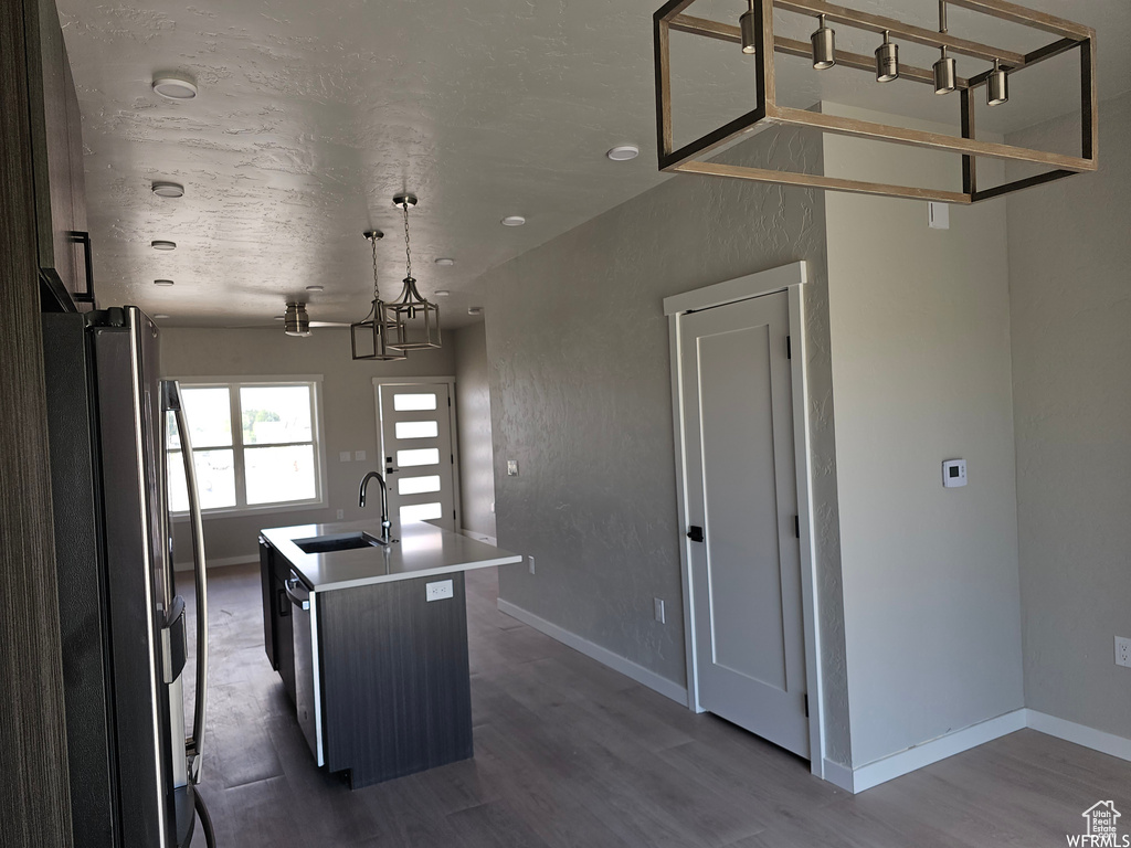 Kitchen with stainless steel refrigerator, dark hardwood / wood-style flooring, a center island with sink, sink, and pendant lighting