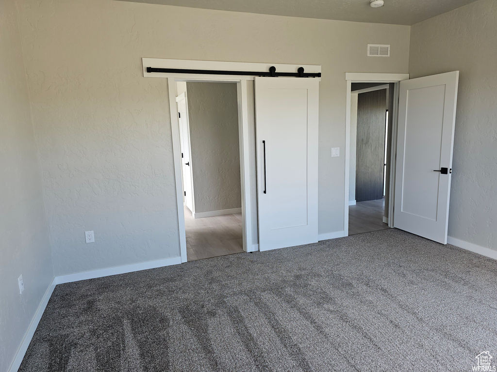 Unfurnished bedroom featuring carpet, a barn door, and a closet