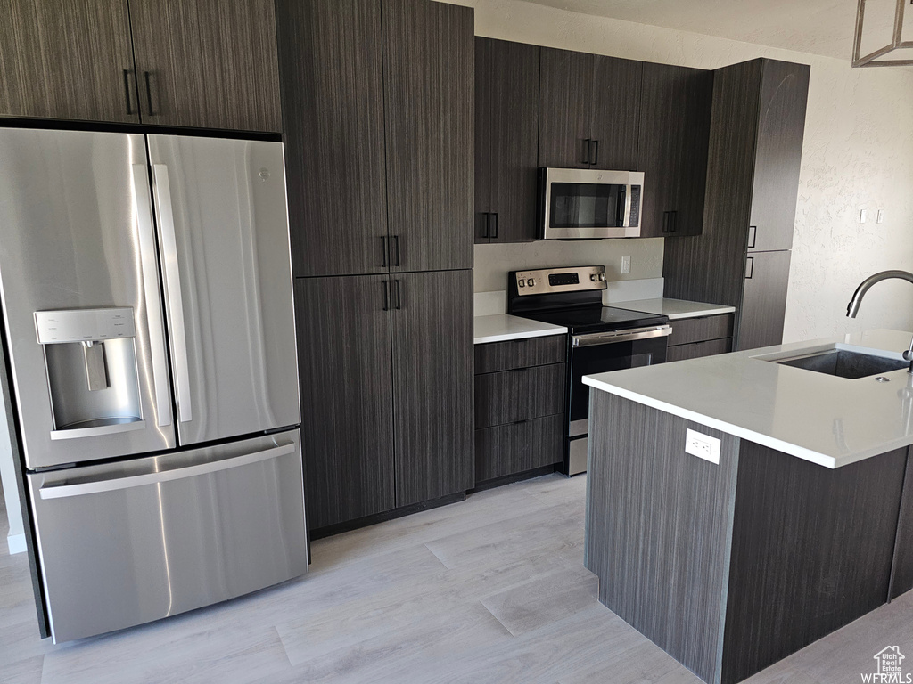 Kitchen featuring an island with sink, sink, light wood-type flooring, and appliances with stainless steel finishes