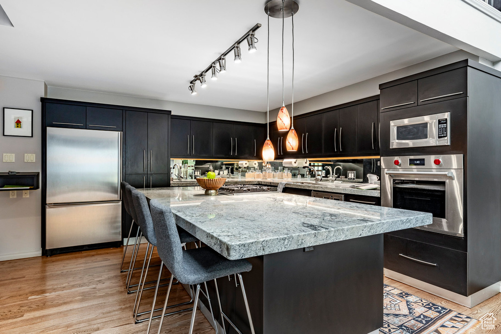 Kitchen with a center island, light wood-type flooring, stainless steel appliances, decorative light fixtures, and track lighting