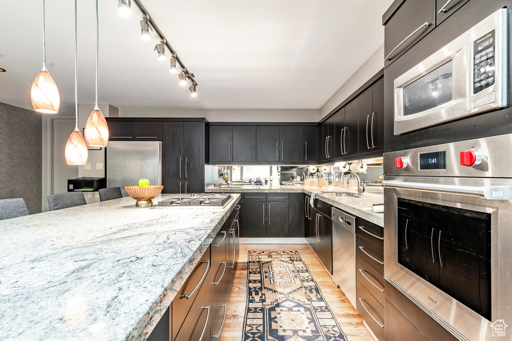 Kitchen featuring light stone countertops, light hardwood / wood-style floors, built in appliances, track lighting, and hanging light fixtures