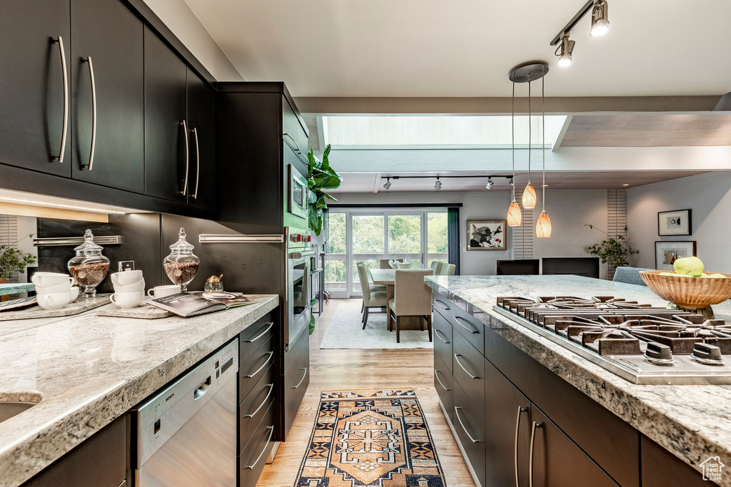 Kitchen with light stone countertops, light wood-type flooring, appliances with stainless steel finishes, decorative light fixtures, and track lighting