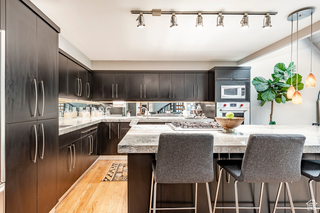 Kitchen with decorative light fixtures, light stone counters, stainless steel appliances, rail lighting, and light wood-type flooring