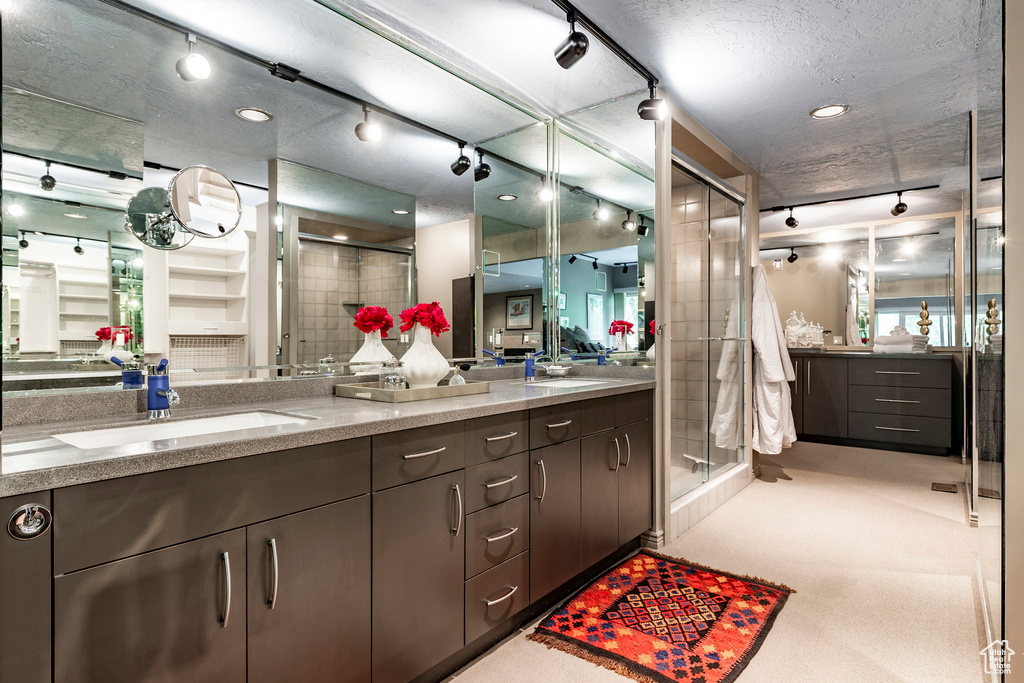 Bathroom with dual sinks, a shower with door, a textured ceiling, track lighting, and large vanity