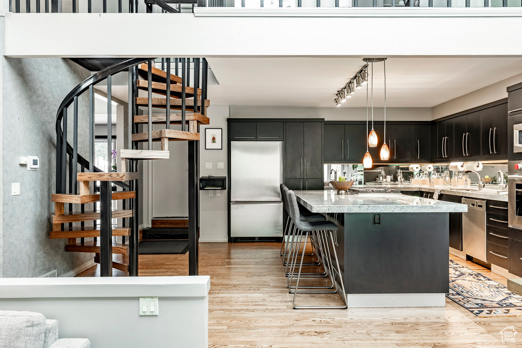 Kitchen with stainless steel appliances, light wood-type flooring, pendant lighting, track lighting, and a breakfast bar