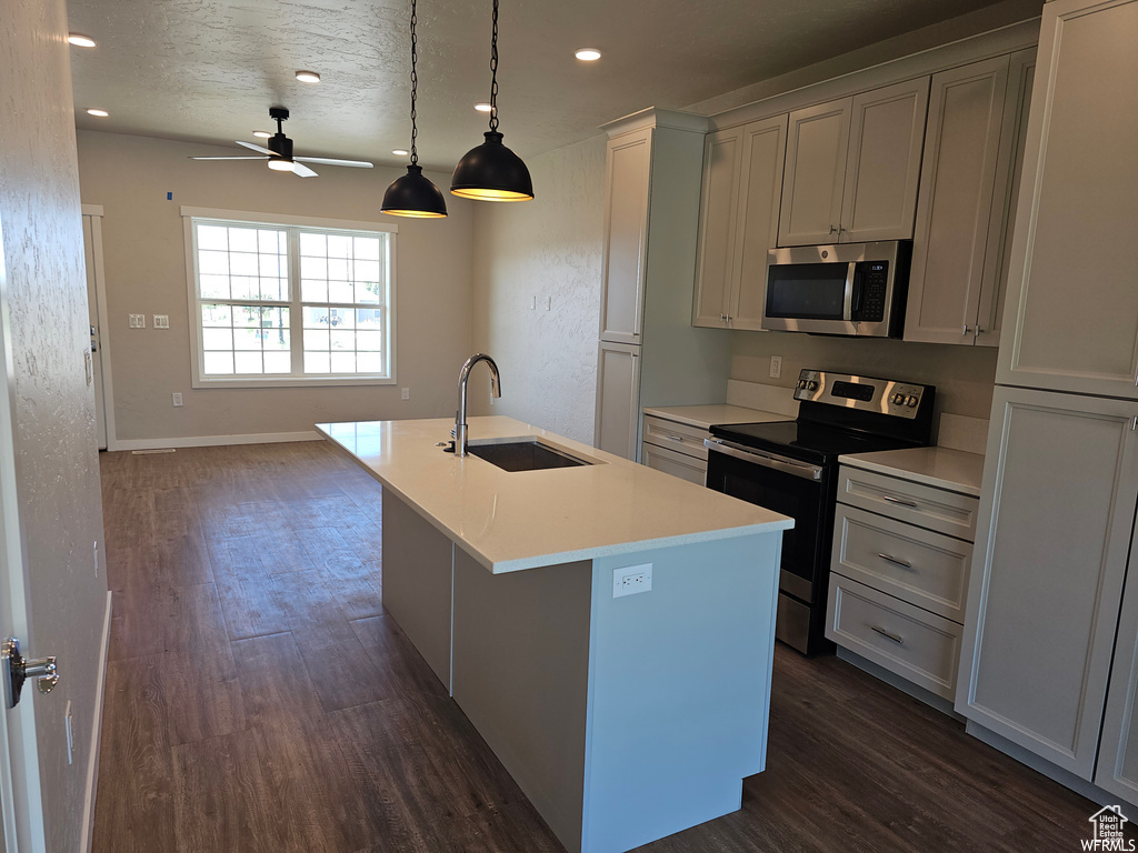 Kitchen with decorative light fixtures, dark hardwood / wood-style flooring, sink, a kitchen island with sink, and appliances with stainless steel finishes