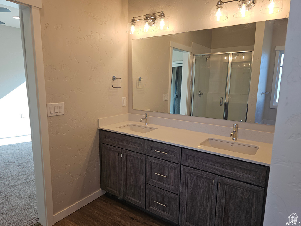 Bathroom with wood-type flooring, walk in shower, double sink, and vanity with extensive cabinet space