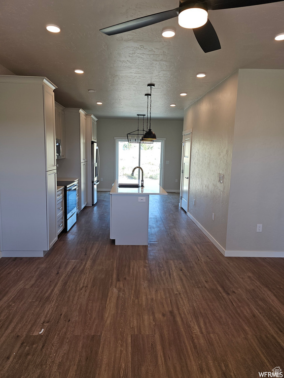 Kitchen with a center island with sink, stainless steel appliances, decorative light fixtures, dark wood-type flooring, and sink