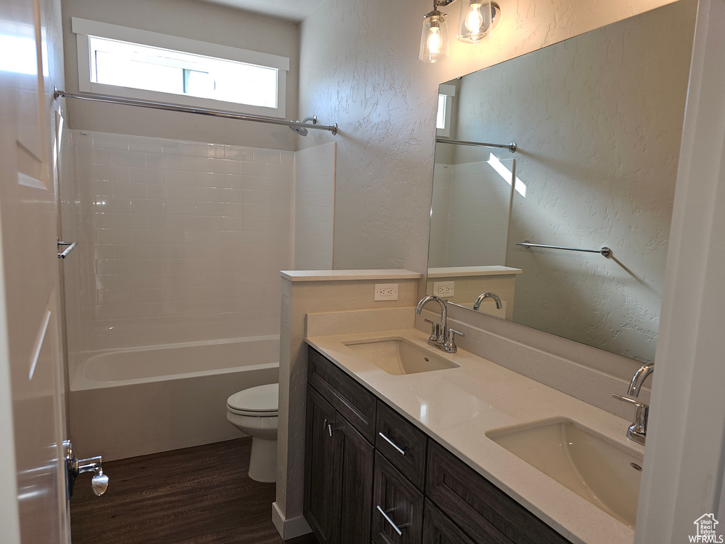 Full bathroom featuring oversized vanity, dual sinks, toilet, shower / bathtub combination, and wood-type flooring