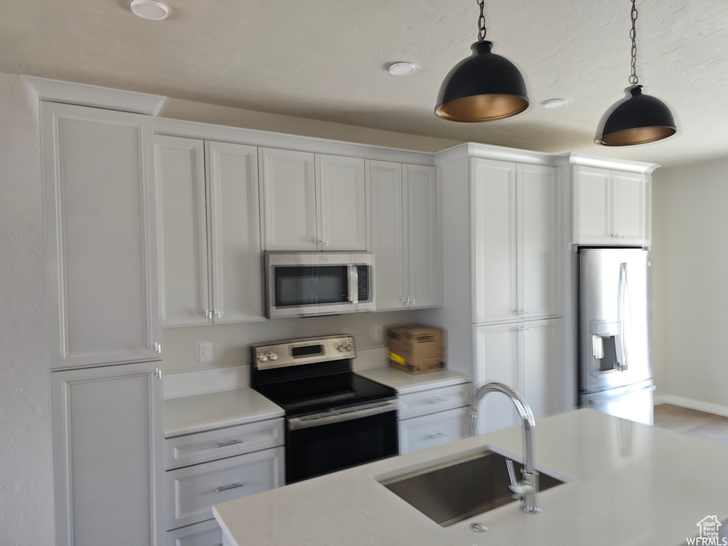 Kitchen featuring stainless steel appliances, white cabinets, sink, and pendant lighting