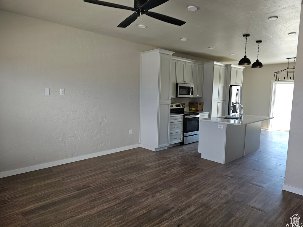 Kitchen featuring stainless steel appliances, decorative light fixtures, dark hardwood / wood-style flooring, and a kitchen island with sink