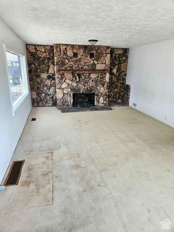 Unfurnished living room with a stone fireplace, carpet, and a textured ceiling