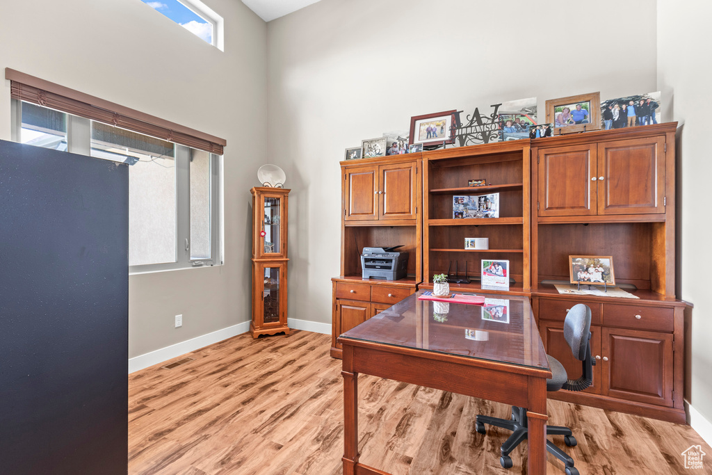 Home office with a towering ceiling and light hardwood / wood-style flooring