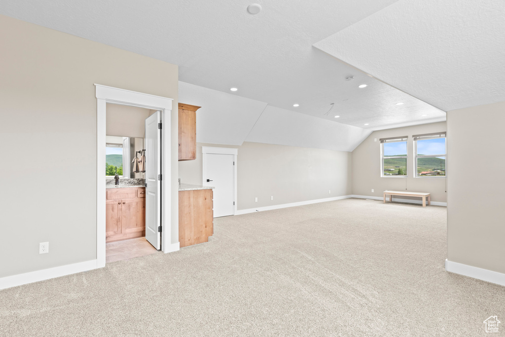 Unfurnished living room featuring light colored carpet, vaulted ceiling, and a textured ceiling