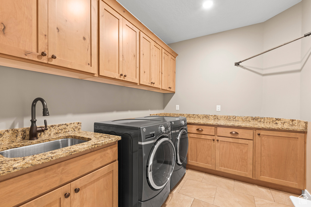 Clothes washing area featuring sink, light tile flooring, cabinets, and washing machine and dryer