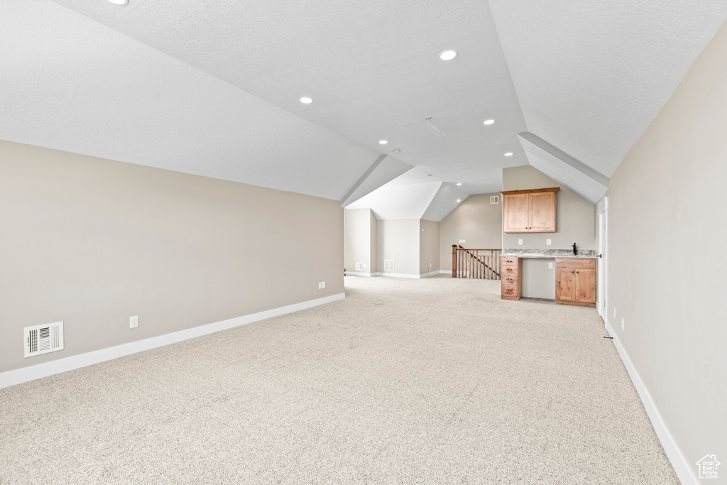 Unfurnished living room featuring light carpet and vaulted ceiling