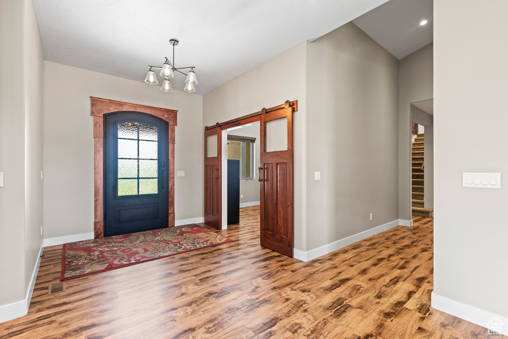 Foyer with vaulted ceiling, hardwood / wood-style floors, a barn door, and a chandelier