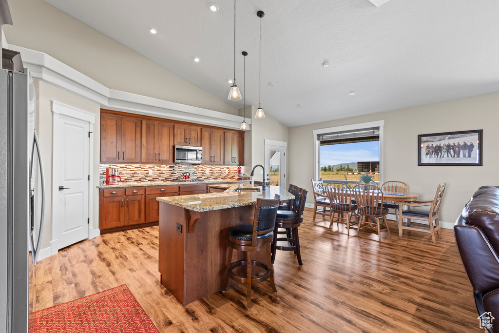 Kitchen featuring hanging light fixtures, light wood-type flooring, light stone countertops, and stainless steel appliances