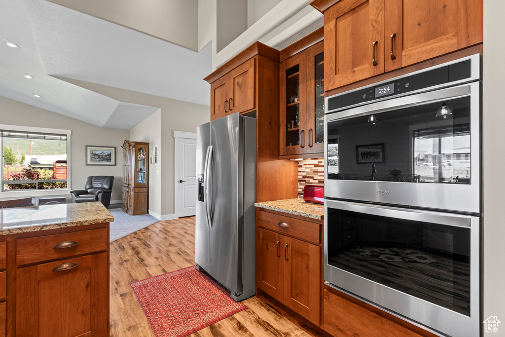 Kitchen with stainless steel appliances, light stone counters, tasteful backsplash, and light hardwood / wood-style flooring