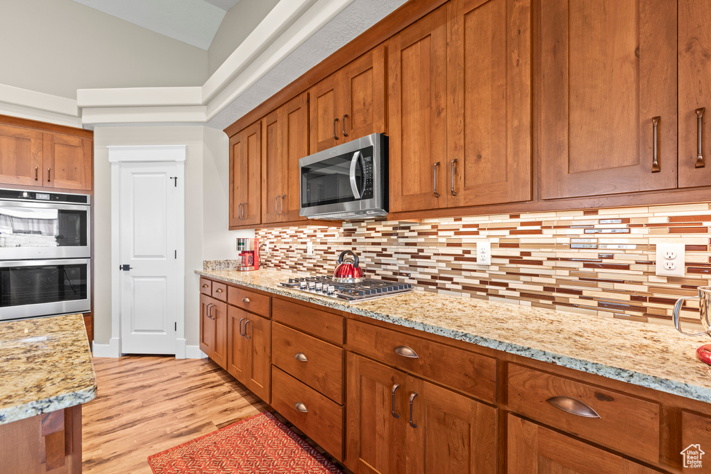 Kitchen featuring lofted ceiling, light wood-type flooring, appliances with stainless steel finishes, light stone counters, and tasteful backsplash