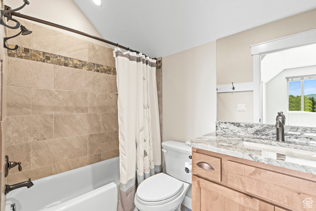 Full bathroom with toilet, large vanity, vaulted ceiling, and shower / bath combo with shower curtain