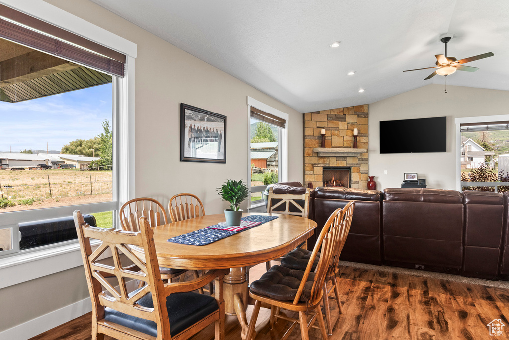 Dining room with a stone fireplace, dark wood-type flooring, lofted ceiling, and ceiling fan